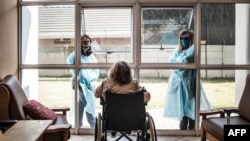 FILE - Relatives chat through a window to a wheelchair-bound woman, a resident of Casa Serena, a home for seniors, in Johannesburg, South Africa, July 22, 2020.