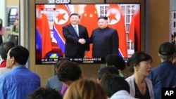 People watch a TV screen showing North Korean leader Kim Jong Un, right, welcoming Chinese President Xi Jinping, at the Seoul Railway Station in Seoul, South Korea, Friday, June 21, 2019. 