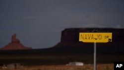 FILE - A sign for Navajo Drive is seen against cloud-darkened Oljato-Monument Valley, Utah, on the Navajo Reservation, April 30, 2020. Across the nation, Native American tribes are working to protect their oldest members from COVID. 