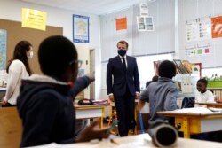 French President Emmanuel Macron, wearing a protective face mask, speaks with schoolchildren during a class at the Pierre Ronsard elementary school, May 5 2020 in Poissy, outside Paris.