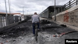 Un hombre monta en bicicleta sobre las cenizas donde se quemó un autobús de transporte público durante una protesta por reformas políticas y contra el gobierno, en Bogotá, el 24 de mayo de 2021.