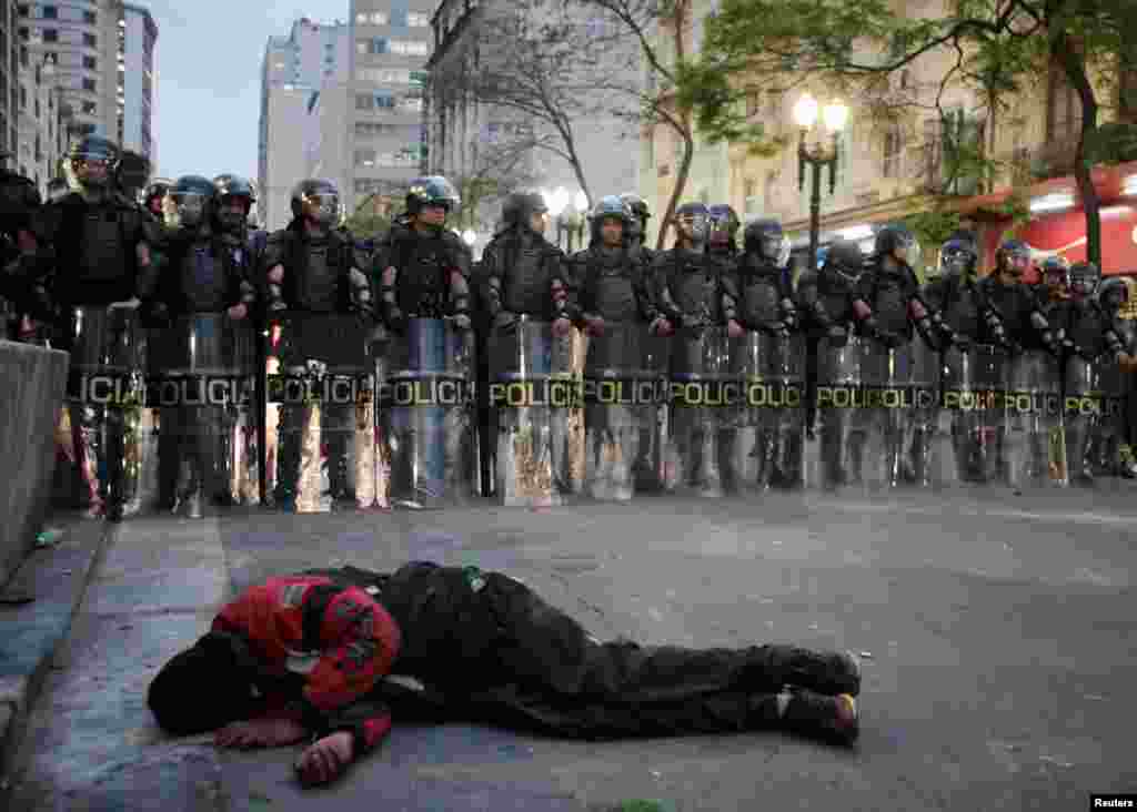 A homeless man sleeps as riot police face off against members of Brazil's Roofless Movement during a protest against their forced eviction from an abandoned building they were occupying, in downtown Sao Paulo, Sept. 16, 2014.