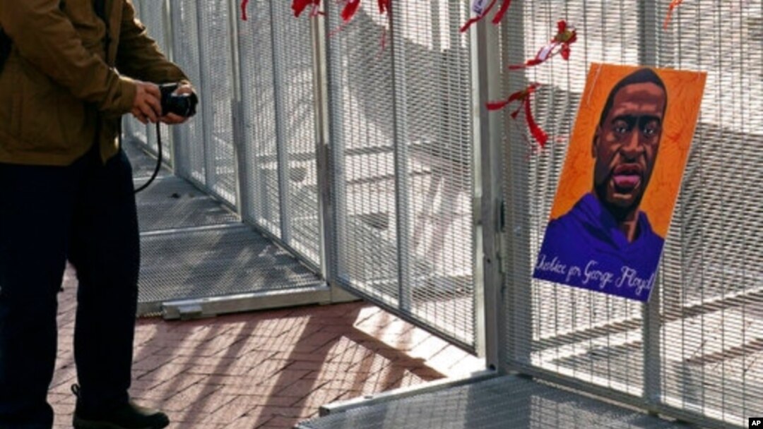 A passerby stops to take a photo of a George Floyd picture hanging on the fence surrounding the Hennepin County Government Center in Minneapolis where the trial of former Minneapolis police Officer Derek Chauvin continues, April 2, 2021.
