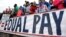 FILE - Fans stand behind a large sign for equal pay for the women's soccer team during a match between the United States and Colombia in East Hartford, Conn. The World Economic Forum's annual Global Gender Gap Report released on Oct. 25, 2016, found that the global gender pay gap will not be closed for another 170 years if current trends continue.