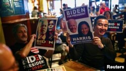 Orang-orang memegang poster yang berisi dukungan terhadap Joe Biden dan Kamala Harris saat mereka menyaksikan penghitungan langsung hasil pemilu presiden AS di salah satu bar di Taipei, Taiwan, pada 4 Novermber 2020. (Foto: Reuters/Ann Wang)