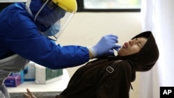 A woman reacts as she has her nasal swab sample collected by a health worker during a mass test for the new coronavirus in Jakarta, Indonesia, June 21, 2020. 