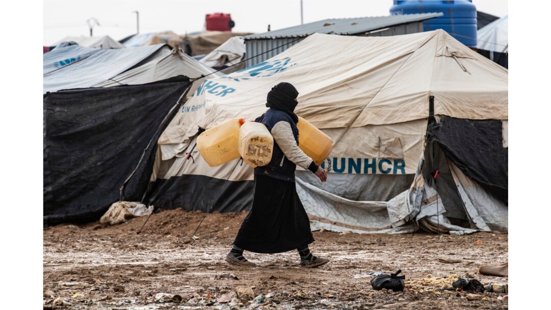 FILE - A woman carries jerry cans to fill them up with water at the al-Hol camp for the displaced where families of Islamic State (IS) foreign fighters are held in northeastern Syria, December 9, 2019.