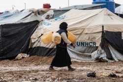 A woman carries jerry cans to fill them up with water at the Kurdish-run al-Hol camp for the displaced where families of Islamic State (IS) foreign fighters are held, in the al-Hasakeh governorate in northeastern Syria on Dec. 9, 2019.