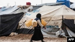 FILE - A woman carries jerry cans to fill them up with water at the Kurdish-run al-Hol camp for the displaced where families of Islamic State (IS) foreign fighters are held, in the al-Hasakeh governorate in northeastern Syria on Dec. 9, 2019.