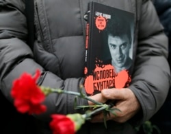 FILE - A visitor holds flowers and a book "Confessions of the Rebel" by Russian leading opposition figure Boris Nemtsov while waiting to attend a memorial service before the funeral of Nemtsov in Moscow, March 3, 2015.