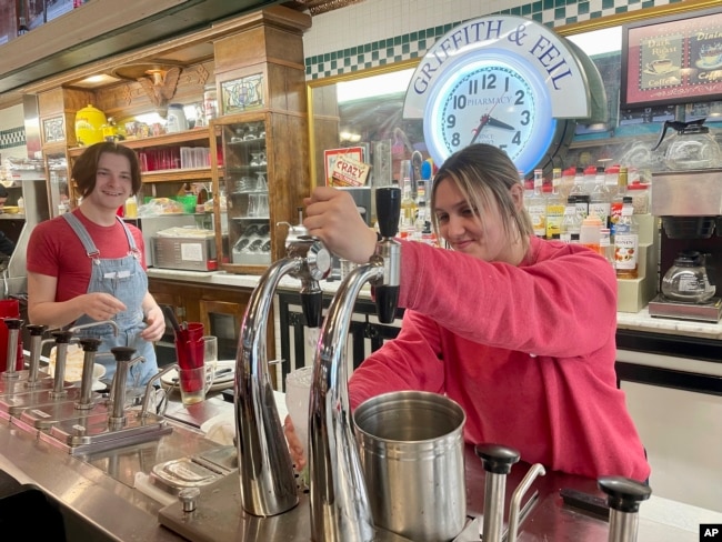 Malli Jarrett, right, serves up drinks from the soda fountain while co-worker Nathaniel Fornash watches at Griffith & Feil Drug on Thursday, March 30, 2023, in Kenova, W. Va. (AP Photo/John Raby)