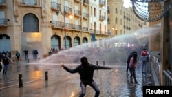 A demonstrator throws a stone as police use a water cannon during a protest against the newly formed government in Beirut, Lebanon January 22, 2020.
