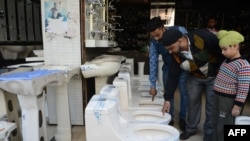 FILE - A store employee shows toilets to customers in a hardware showroom in Amritsar, India, Nov. 18, 2017.