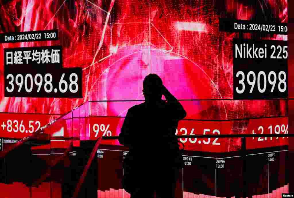 A visitor using his smartphone takes photos of an electronic screen displaying Japan&#39;s Nikkei share average, which surged past an all-time record high scaled in December 1989, inside a building in Tokyo, Japan.