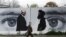 FILE - An Afghan man wearing a protective face mask walks past a wall painted with images of Zalmay Khalilzad, U.S. envoy in Afghanistan, and Mullah Abdul Ghani Baradar, the leader of the Taliban delegation, in Kabul, Afghanistan, April 13, 2020.