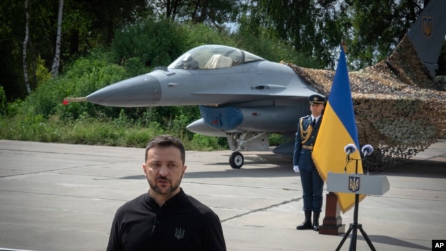 Президент України Володимир Зеленський виступає на тлі винищувачів F-16 ЗСУ в невідомому місці в Україні, 4 серпня 2024 р. (Фото: AP Photo/Єфрем Лукацький)