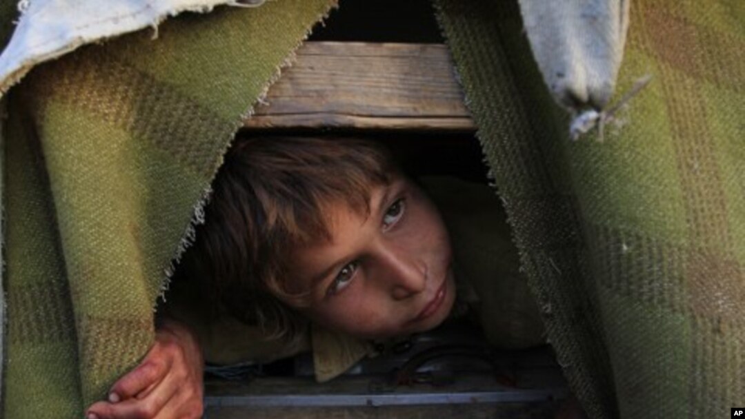 An Afghan refugee boy, Gul Zaman, who fled from Afghanistan with his family, peeps from his make-shift tent in the outskirts of Karachi, Pakistan, March 13, 2012. 