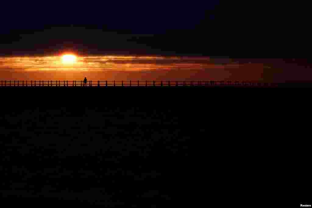 People look on as the sun rises during Summer Solstice, as seen from Roker Beach in Sunderland, Britain.