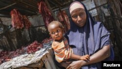 A Somali woman selling meat from a kiosk holds her child in a market area in the centre of the southern Somali port city of Kismayo, October 7, 2012.