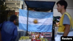 Ciudadanos caminan por las calles de Buenos Aires, frente a una bandera argentina expuesta en un puesto callejero, el 12 de diciembre de 2023.