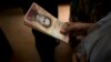 A customer holds a stack of 100-bolivar notes at a bakery in downtown Caracas, Venezuela, Dec. 12, 2016. Venezuelans were rushing to spend their 100-bolivar notes after a surprise announcement that they will be taken out of circulation. More of the new 500-bolivar notes arrived in Venezuela, Dec. 28, 2016. 