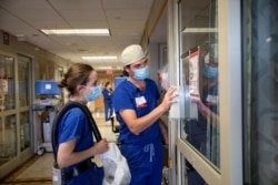 Nurse Joseph Bertram and Physical Therapist Elizabeth Tewes talk to a nursing colleague through the slightly opened door of a room housing a coronavirus disease (COVID-19) patient in Madison, WI.