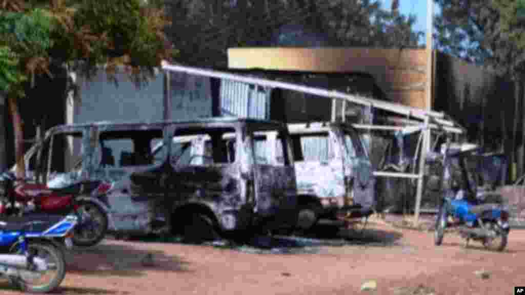 People walk past vehicles and shops burnt by Boko Haram Islamists on a street of Benisheik.