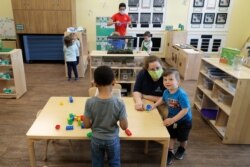 In this May 27, 2020, photo, teachers Jana Blair, right, and Aaron Rainboth, upper-center, wear masks as they work with kids at the Frederickson KinderCare daycare center, in Tacoma, Wash.