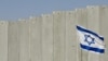 FILE - An Israeli flag is planted in front of Israel's separation barrier in the West Bank village of Abu Dis, on the outskirts of Jerusalem, July 7, 2004. 