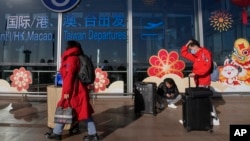 Travelers wearing face masks with their luggage walk through the international flight departure terminal entrance gate at the capital airport in Beijing on Dec. 29, 2022.