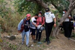 Honduran migrants react while accompanied by a police officer after Guatemalan security forces cleared a road where the migrants have been camping after authorities halted their trek to the United States, in Vado Hondo, Guatemala, Jan. 18, 2021.