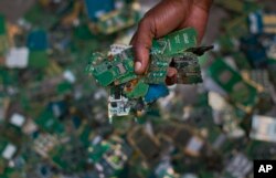 FILE—In this photo taken August18, 2014, a worker gathers handfuls of cellphone printed circuit boards for recycling, at the East African Compliant Recycling facility in Machakos, near Nairobi, in Kenya.