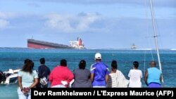 Des passants regardent le vraquier MV Wakashio qui s'était échoué près du parc marin de Blue Bay, dans le sud-est de l'île Maurice, le 6 août 2020. (Photo: Dev Ramkhelawon / L'Express Maurice / AFP)