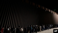 FILE—People line up against a border wall as they wait to apply for asylum after crossing the border from Mexico July 11, 2023, near Yuma, Arizona.