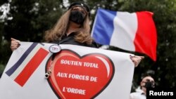 Seorang pendukung polisi, mengenakan topeng pelindung, di depan markas polisi Perancis di Paris, 27 Juni 2020. Spanduk itu berbunyi: "Dukungan total untuk pasukan polisi." (Foto: Reuters)