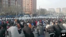 Pengunjuk rasa berhadapan dengan petugas keamanan berpakaian APD putih di kompleks pabrik yang dioperasikan oleh Foxconn Technology Group di Zhengzhou, provinsi Henan, China, 23 November 2022. (AP)