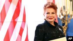 FILE - Georgette Mosbacher stands next to an American flag after receiving her credentials as new United States ambassador to Poland in Warsaw, Sept. 6, 2018. 