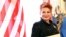 FILE - Georgette Mosbacher stands next to an American flag after receiving her credentials as new United States ambassador to Poland in Warsaw, Sept. 6, 2018. 