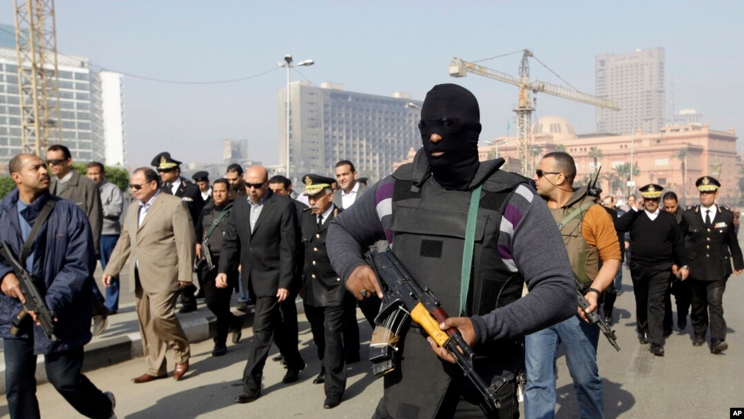 Seorang polisi dengan menggunakan masker mengawal kepala keamanan Kairo, Osama al-Saghir (tiga dari kiri) saat berada di Lapangan Tahrir, pusat pergolakan tahun 2011 di Kairo, Sabtu (25/1).