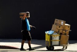 In this Oct. 1, 2020, photo an Amazon worker wears a mask and gloves as he delivers boxes downtown Los Angeles.