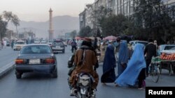 Sekelompok perempuan yang mengenakan burqa tampak menyeberang jalan saat anggota pasukan Taliban bergerak melewati mereka di Kabul, pada 9 Oktober 2021. (Foto: Reuters/Jorge Silva)