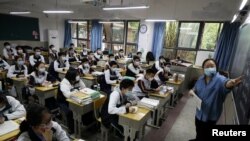 Seorang guru dan siswa sekolah menengah atas yang mengenakan masker di dalam ruang kelas pada hari pertama mereka kembali ke sekolah setelah wabah Covid-19, di Wuhan, Provinsi Hubei, Cina 6 Mei 2020. (Foto: Reuters)