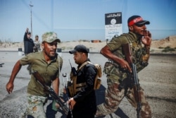 FILE - A members of Iraqi Popular Mobilization Forces (PMF) walk past a poster of PMF members at Popular Mobilization Forces Media Center in Baghdad, Iraq, July 2, 2019.