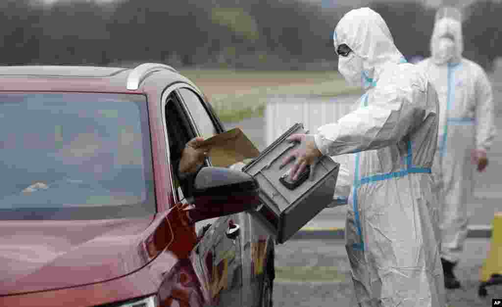 An election committee member, wearing a protective suit, holds a ballot box for a man to vote in regional and senate elections at a drive-in polling station in Prague, Czech Republic.