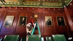 Bethany Gill climbs a ladder to wind a clock in a Pennsylvania Senate hearing chamber, in Harrisburg, Pennsylvania, Dec. 13, 2024. It's one of 273 clocks in Pennsylvania's ornate state Capitol complex buildings that must be wound by hand.