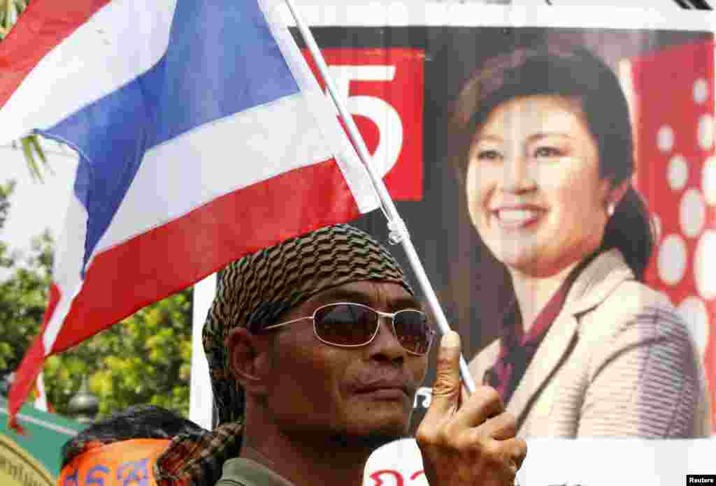 An anti-government protester holds a national flag in front of a portrait of Thailand&#39;s Prime Minister Yingluck Shinawatra, during a rally, Bangkok, Jan. 29, 2014.