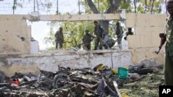 FILE – Soldiers stand near the wreckage of a car bomb that was detonated at the gates of a government office complex in the capital Mogadishu, April 14, 2015.