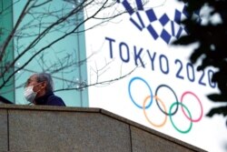 A man wearing a protective mask to help curb the spread of the coronavirus walks near the banner for the Tokyo 2020 Olympic Games in Tokyo, Feb. 25, 2021.