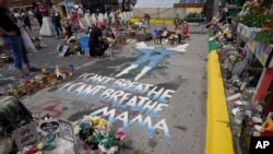 FILE - A woman kneels to weep at the spot where George Floyd was killed, as people gather during the sentencing hearing of former Minneapolis police officer Derek Chauvin for Floyd's murder, in Minneapolis, June 25, 2021.