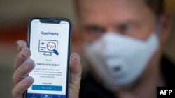 A man holds a smartphone showing a tracking and tracing app launched by the National Institute of Public Health to try to halt a return of the new coronavirus, on April 17, 2020 in Oslo. - Norway, one of the first European countries to begin lifting…